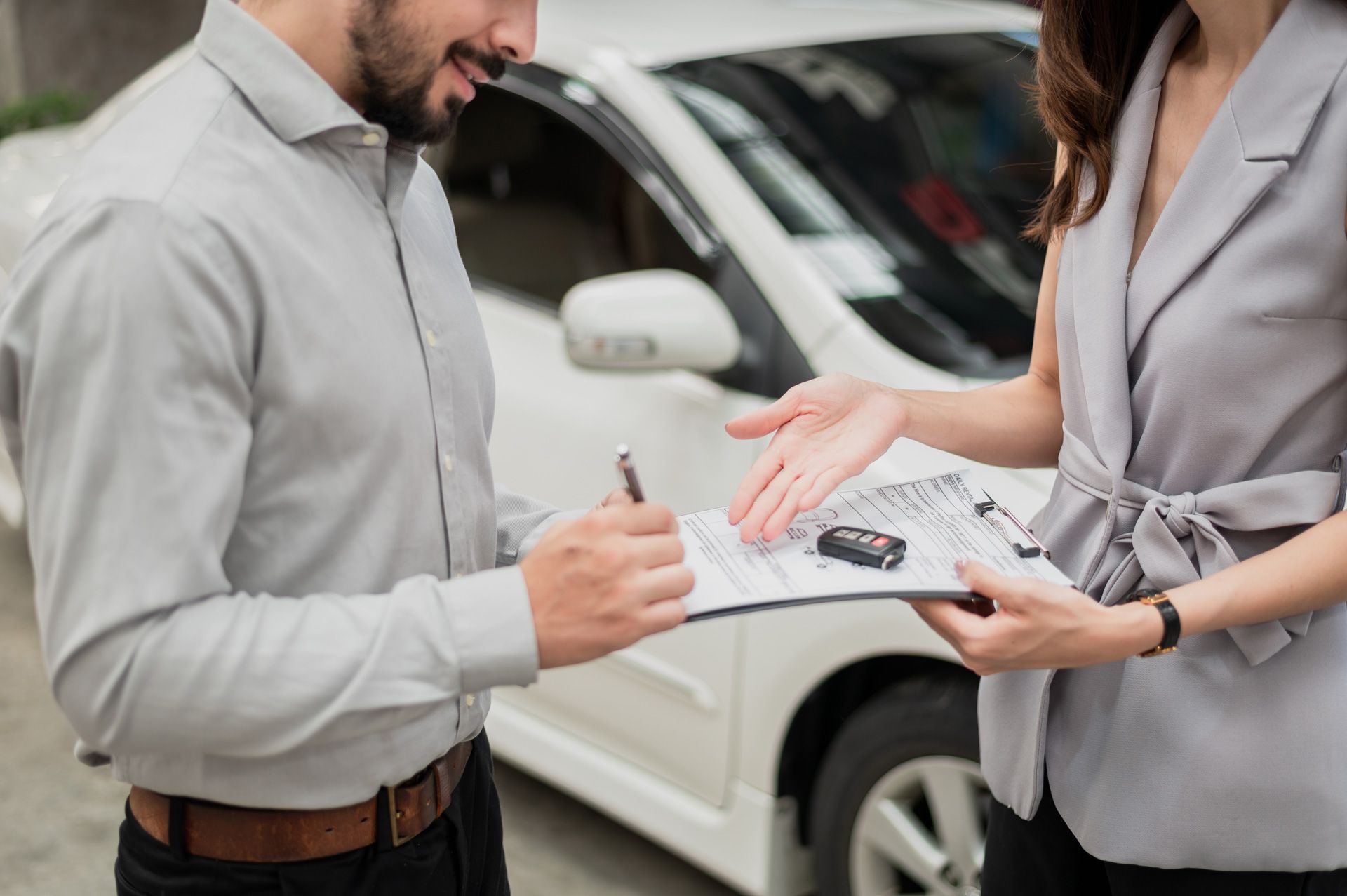 A man and a woman are signing a document in front of a car .