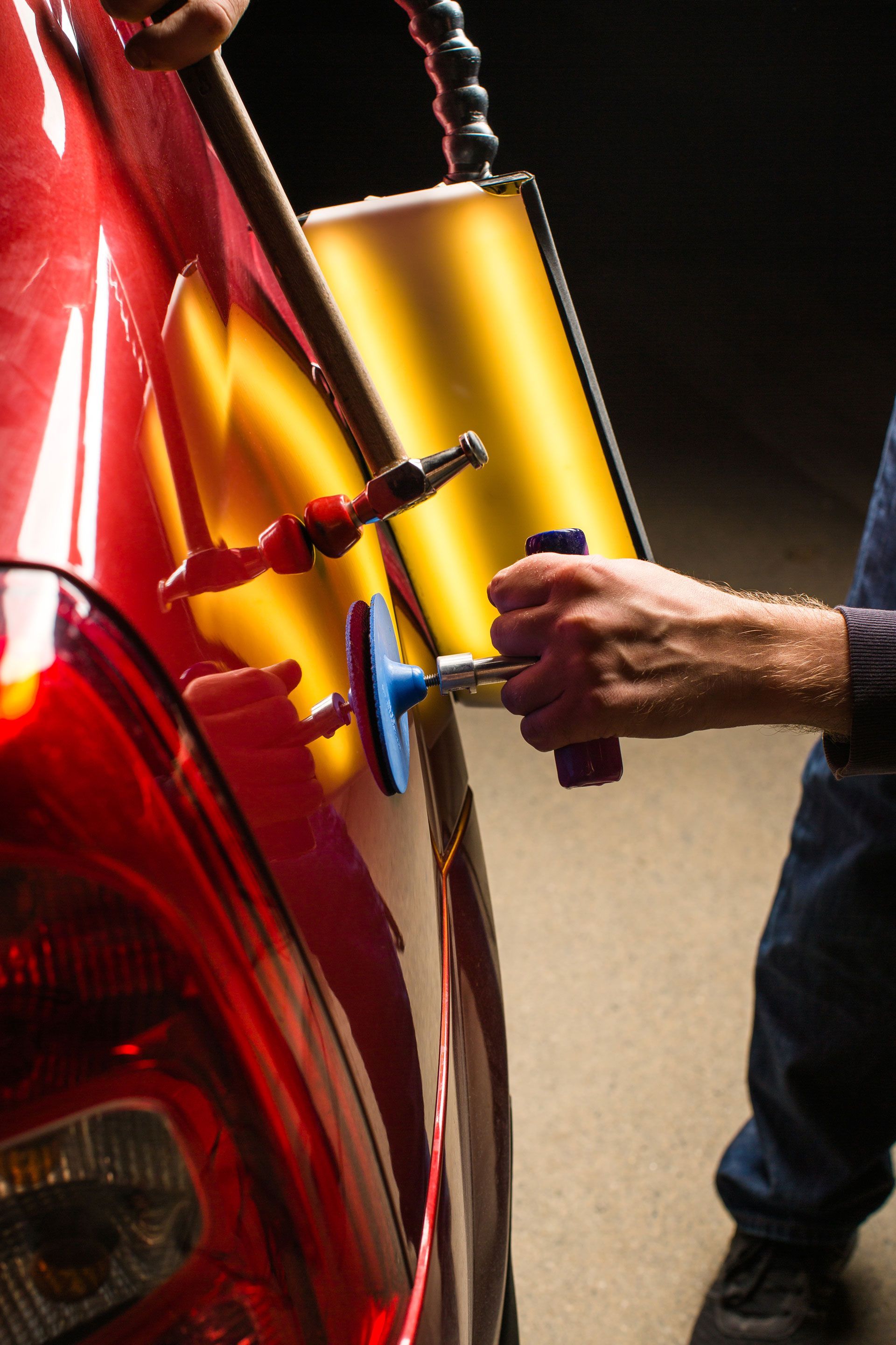 A man is using a tool to fix a dent on a red car .