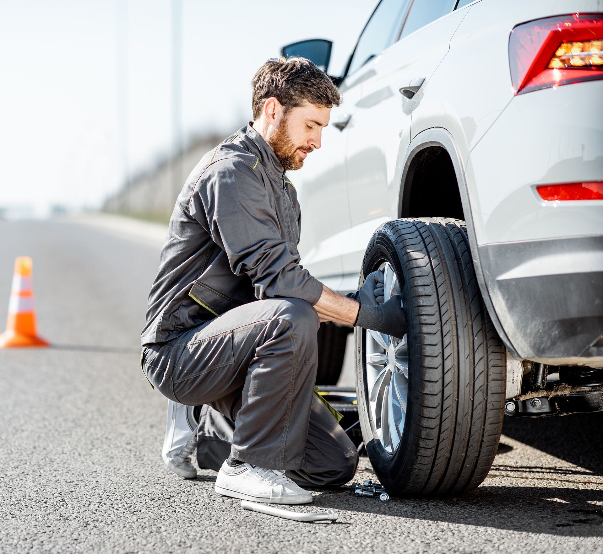 A man is changing a tire on a car on the side of the road.