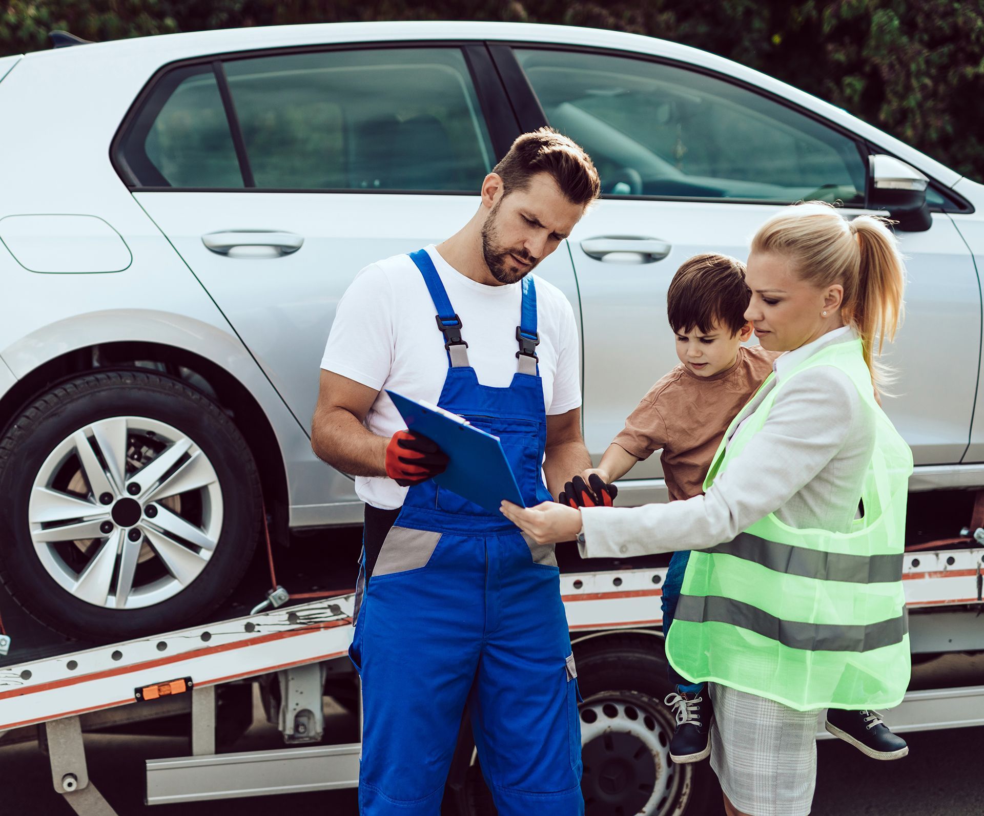A man and a woman are standing next to a tow truck with a car on it.
