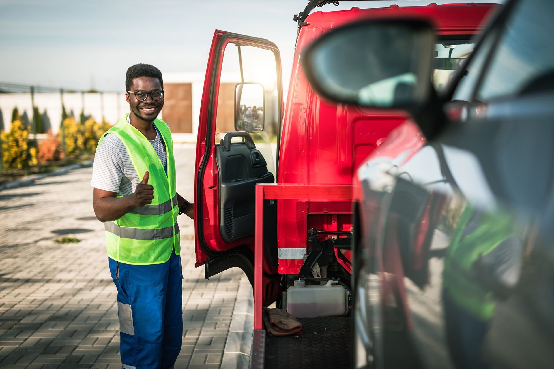 A man is standing next to a tow truck and giving a thumbs up.