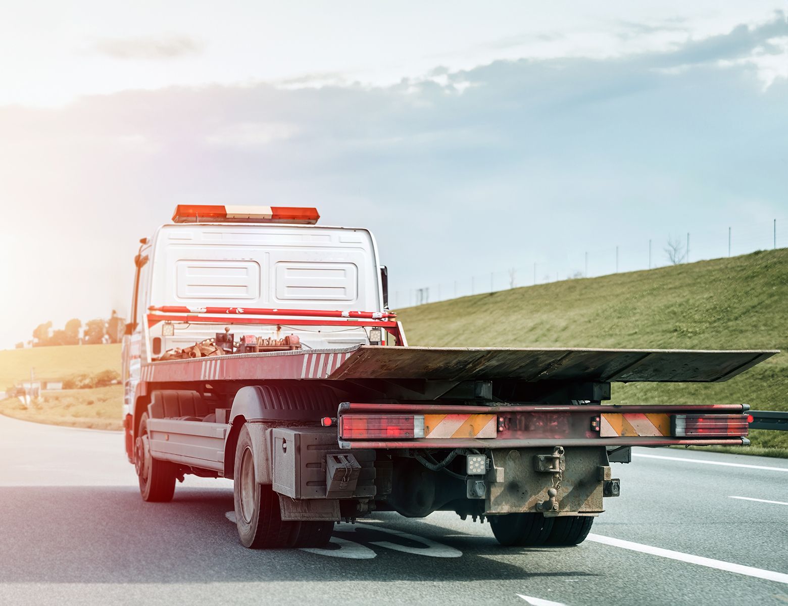 A tow truck with a flat bed is driving down a highway.