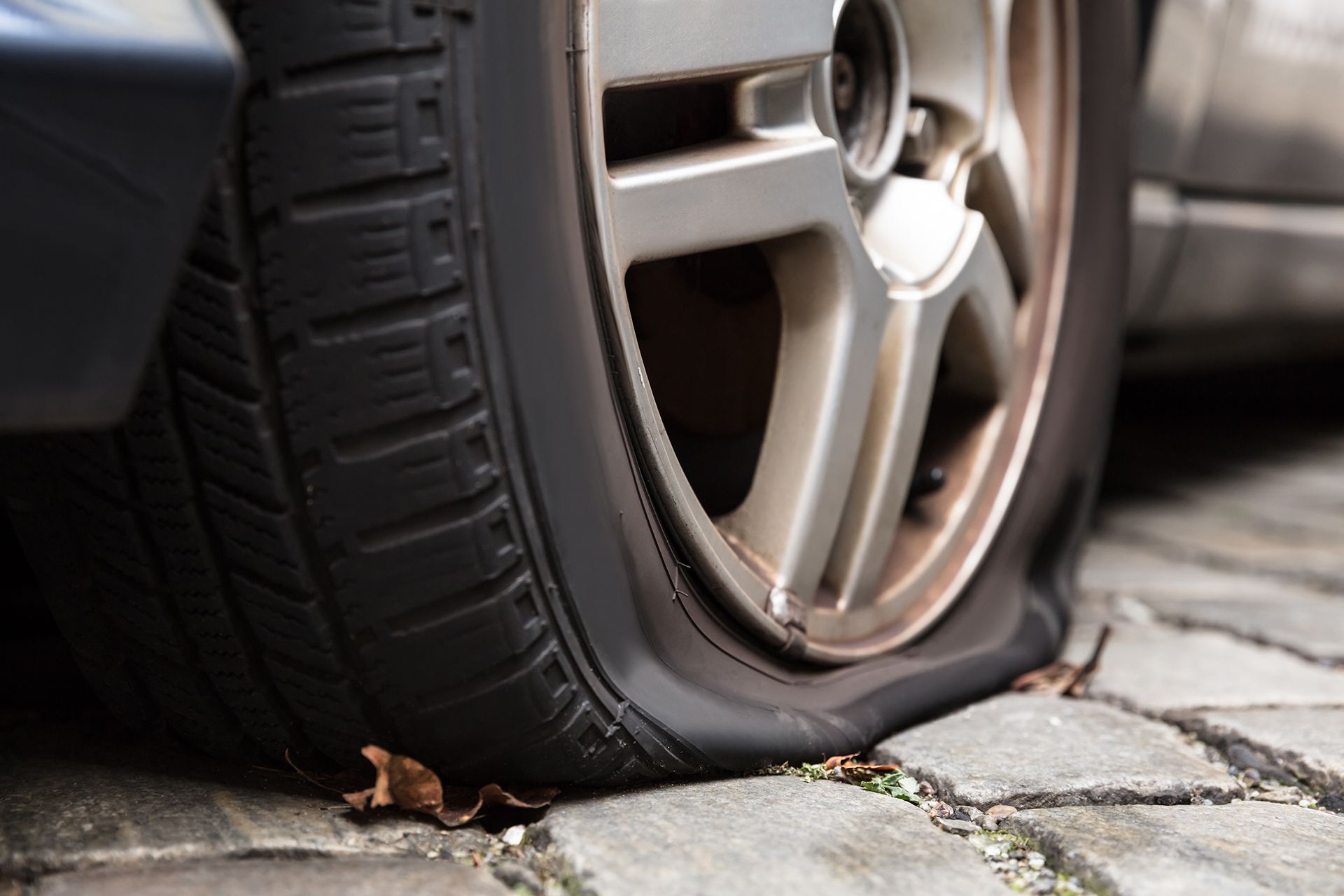 A car with a flat tire is parked on a cobblestone street.