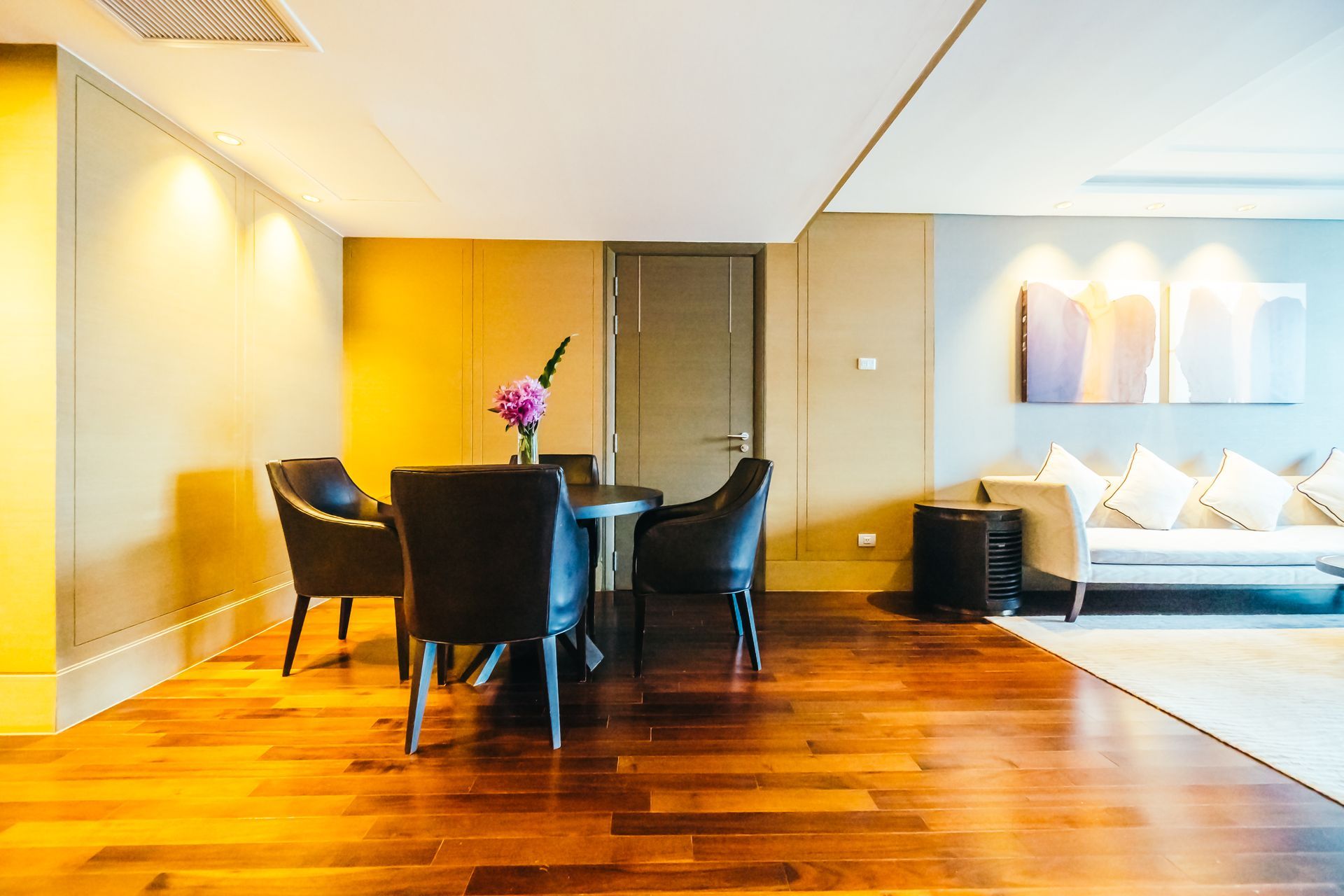 Modern dining area with dark chairs around a round table, wooden floors, and a sofa in the adjacent living space.