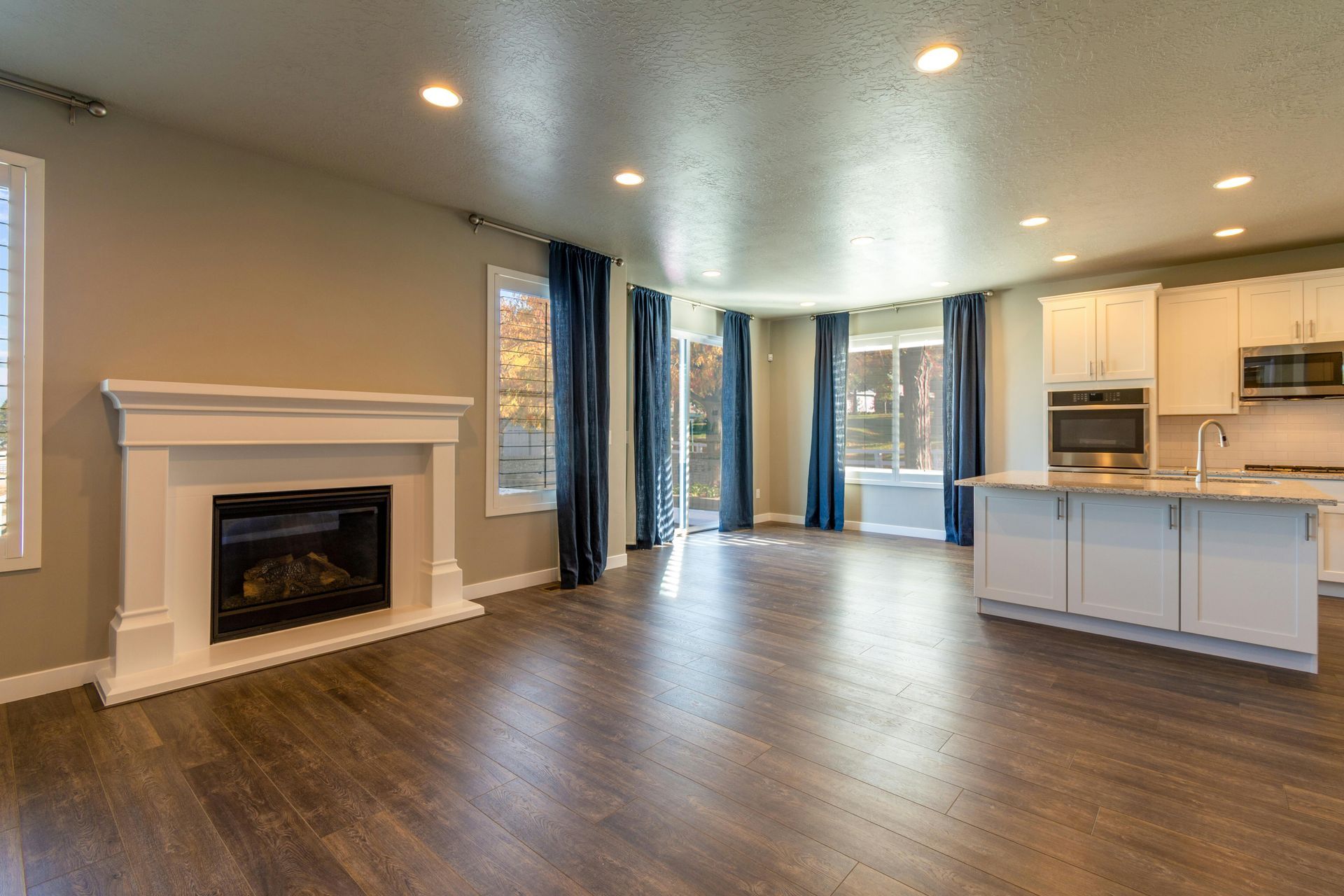 Modern white kitchen with wooden countertops, gray flooring, two windows, and hanging pendant lights over a small table.
