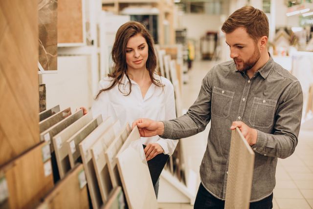 A couple looks at tile samples in a home improvement store, discussing their home renovation choices.