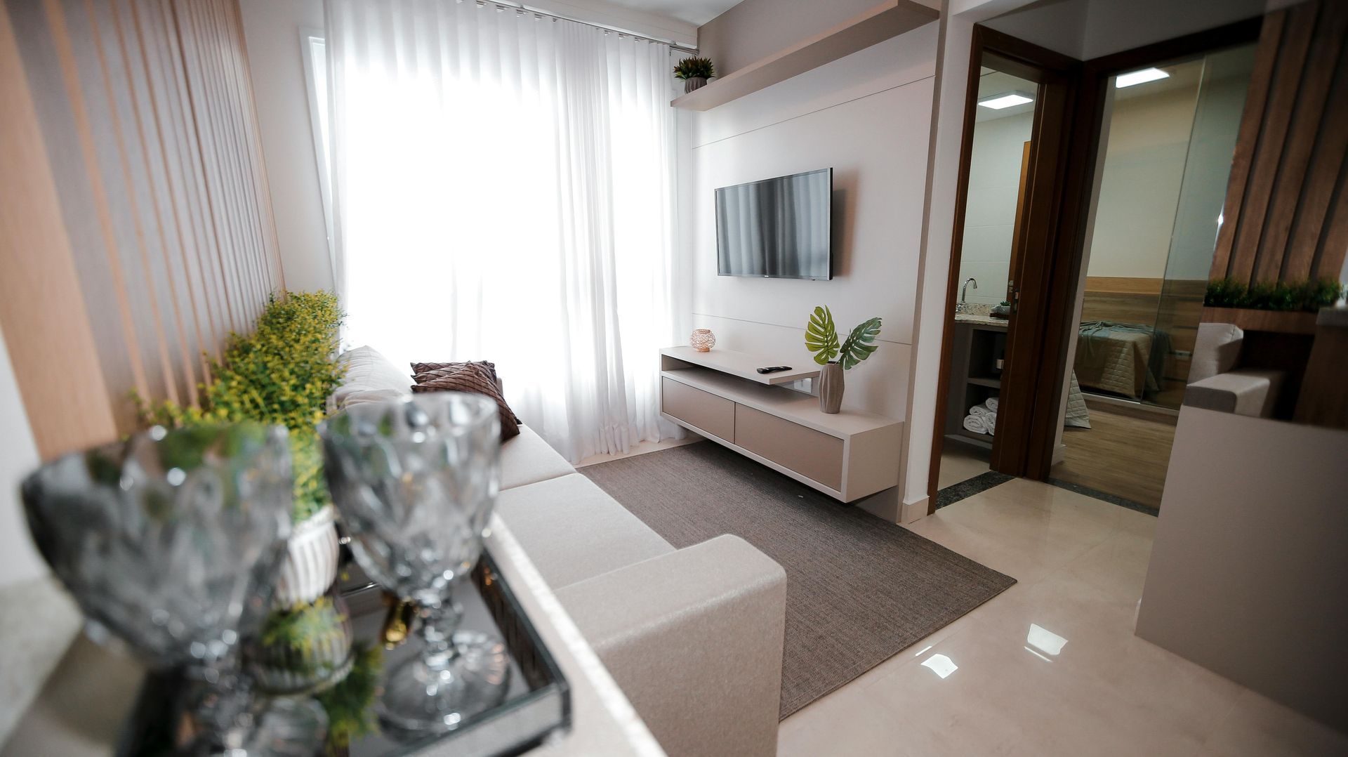 A modern living room with hardwood floors, a dark sofa, a coffee table, and large windows overlooking autumn trees.