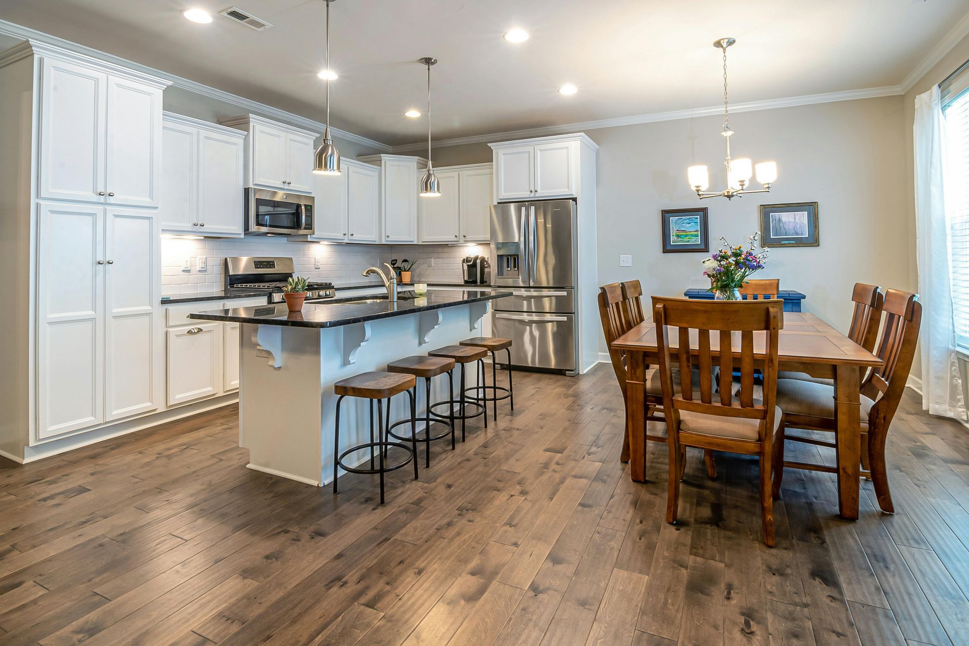 Modern white kitchen with wooden countertops, gray flooring, two windows, and hanging pendant lights over a small table.