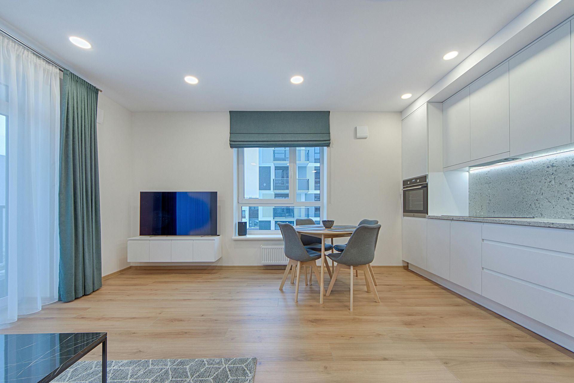 Modern white kitchen with wooden countertops, gray flooring, two windows, and hanging pendant lights over a small table.