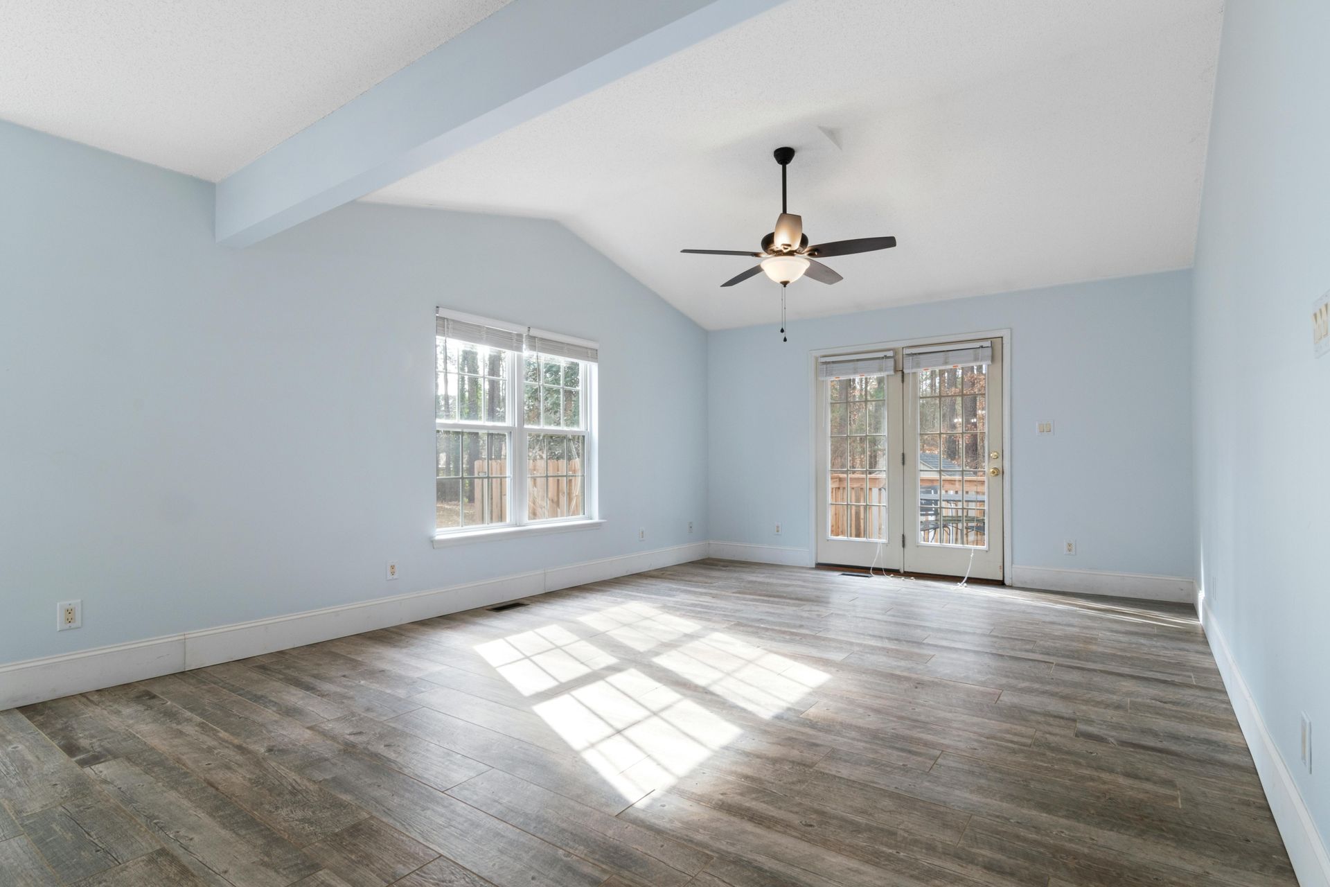 A modern living room with hardwood floors, a dark sofa, a coffee table, and large windows overlooking autumn trees.