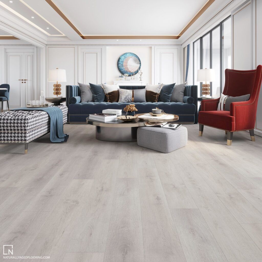 A modern living room with light gray wood flooring, a blue sofa, a red armchair, and a patterned ottoman.