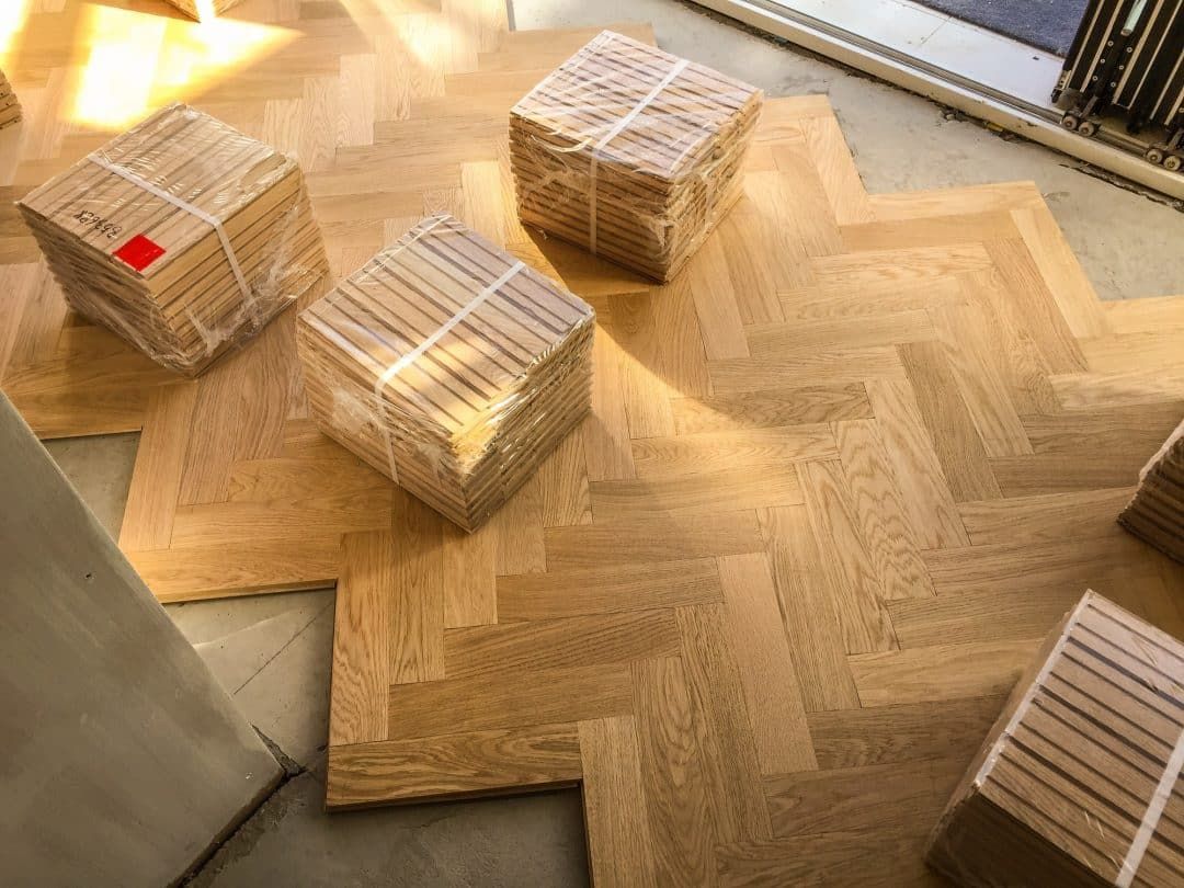 Herringbone pattern wooden parquet floor installation with several bundled stacks of wood planks resting on top.