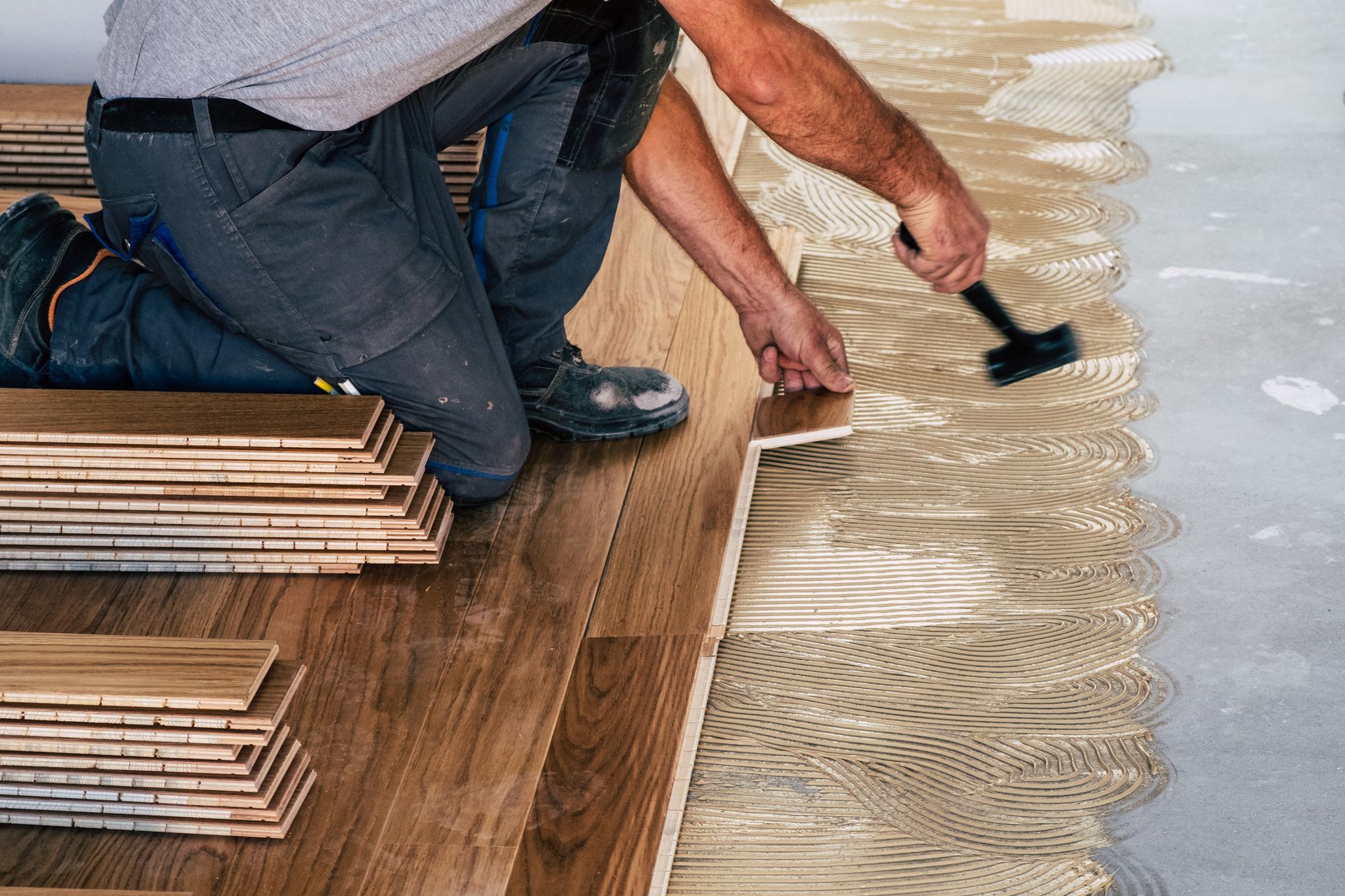 A man is kneeling down and applying glue to a wooden floor.
