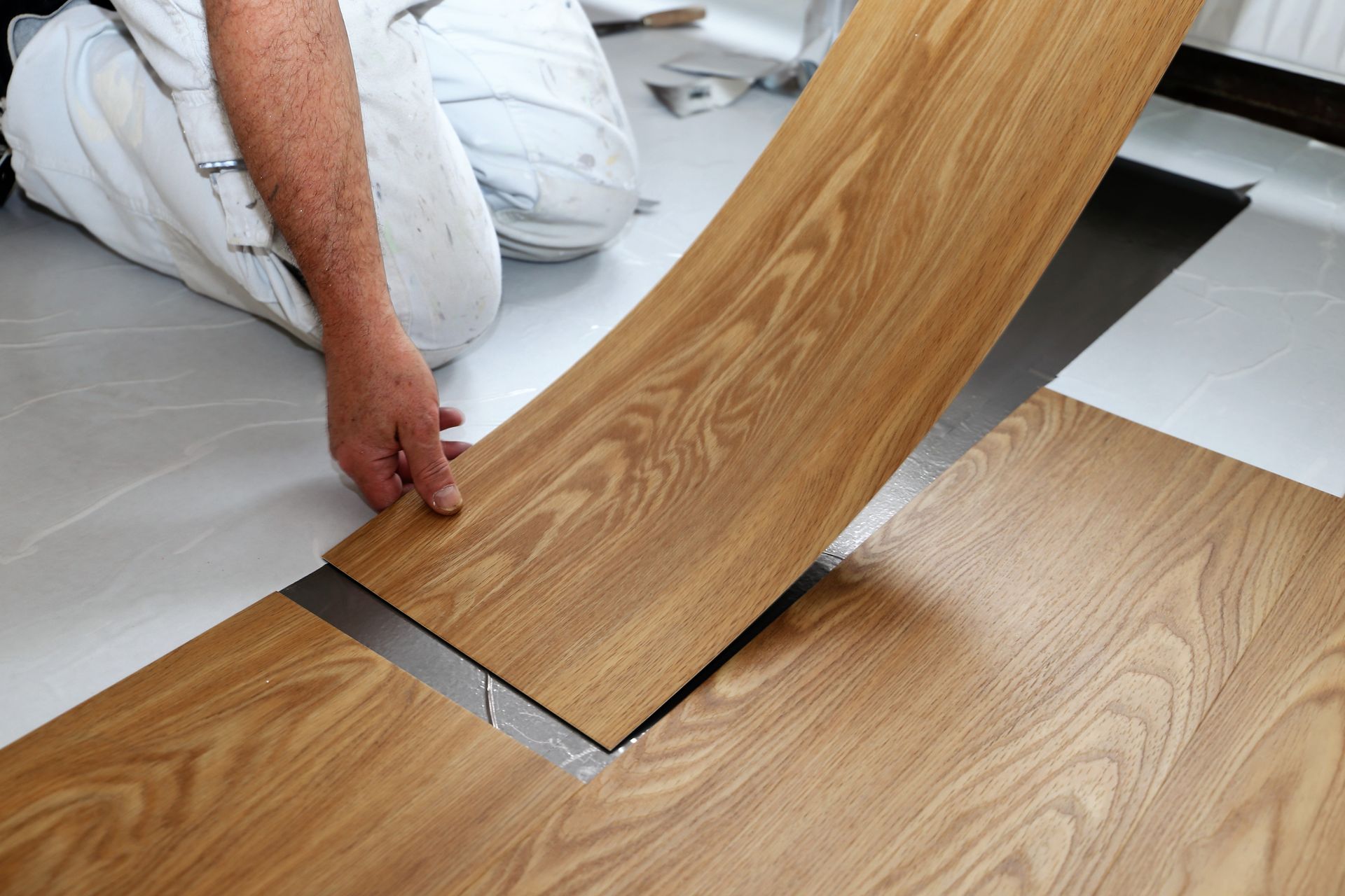 A man is laying a piece of vinyl flooring on the floor.