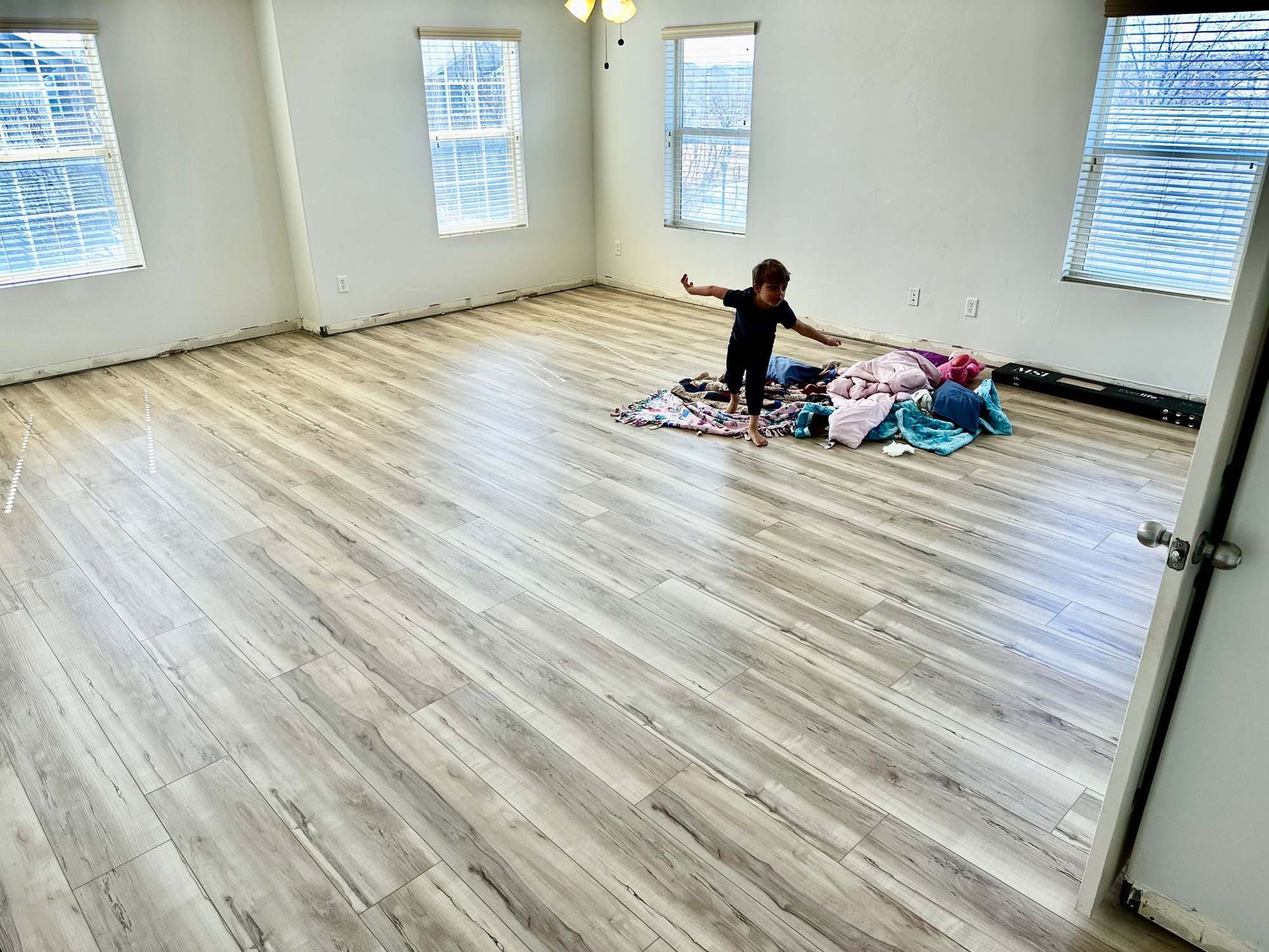 A little girl is standing on a wooden floor in a room.
