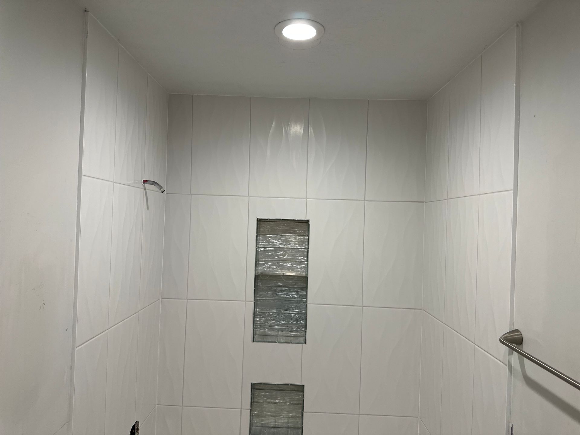 A bathroom with white tiles and a shower head.
