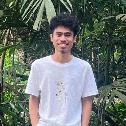 Woman with sleek hair, wearing hoop earrings, flushed cheeks, orange background.