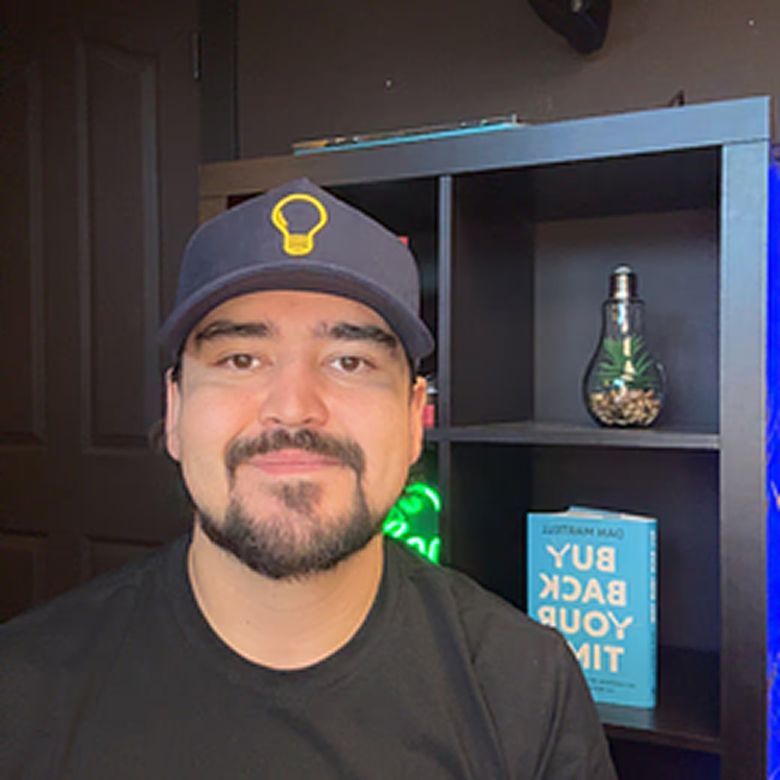 Woman with slicked-back hair and large hoop earrings, posing in front of an orange background.