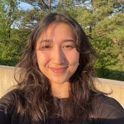 Woman with slicked-back hair and large hoop earrings, illuminated by sunlight on an orange background.