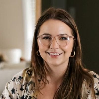 Woman with slicked-back hair and large gold hoop earrings, against a warm orange background, sun-kissed makeup.