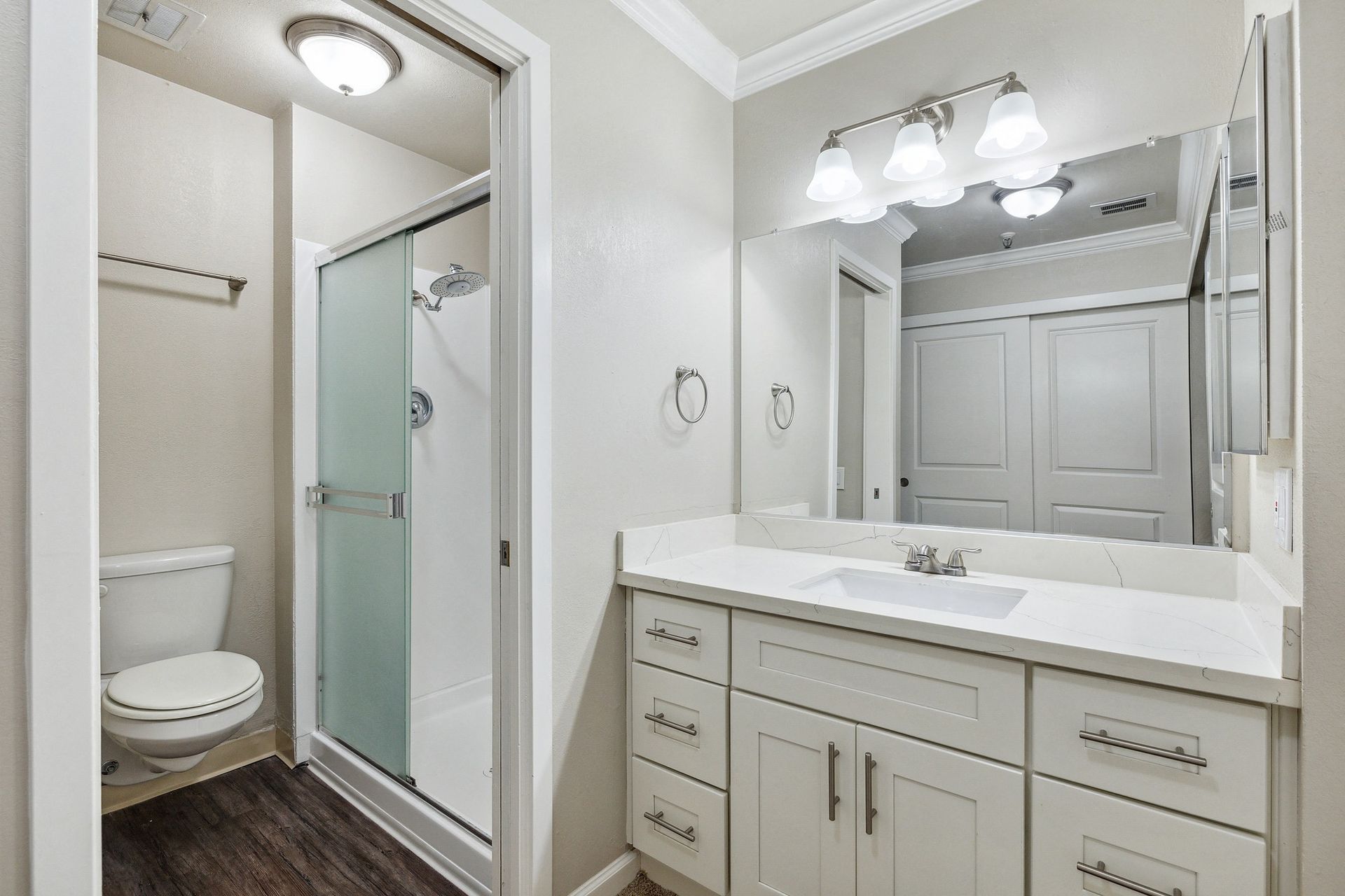 Bathroom in apartment with white vanity, large mirror, and glass shower enclosure.