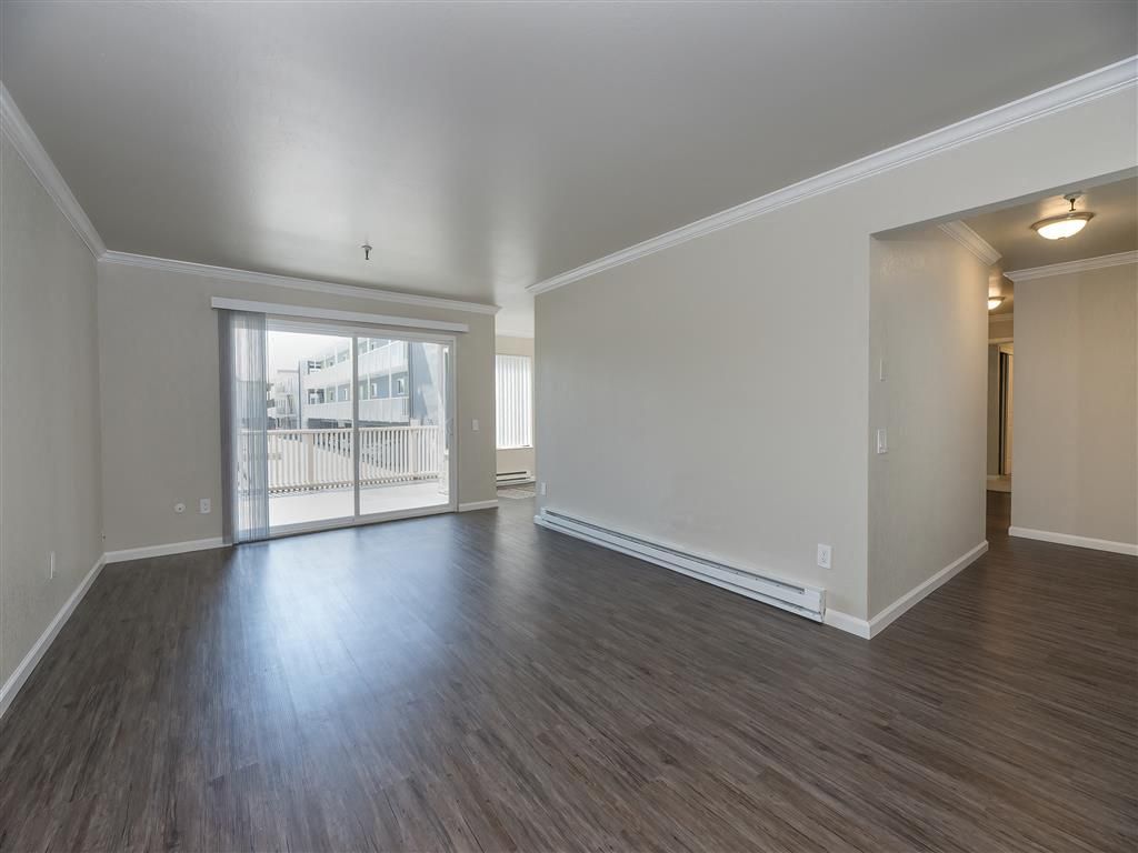 Living room with sliding glass door to balcony, light walls, and dark laminate flooring.