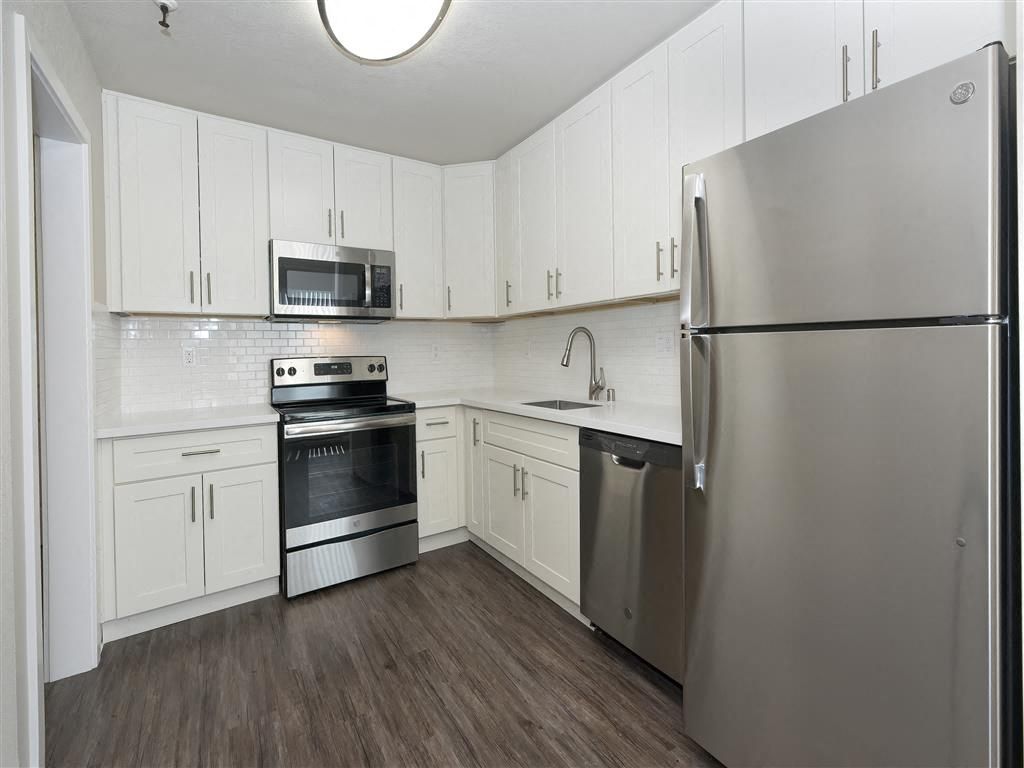 Modern white kitchen with stainless steel fridge, range, microwave, and dishwasher.