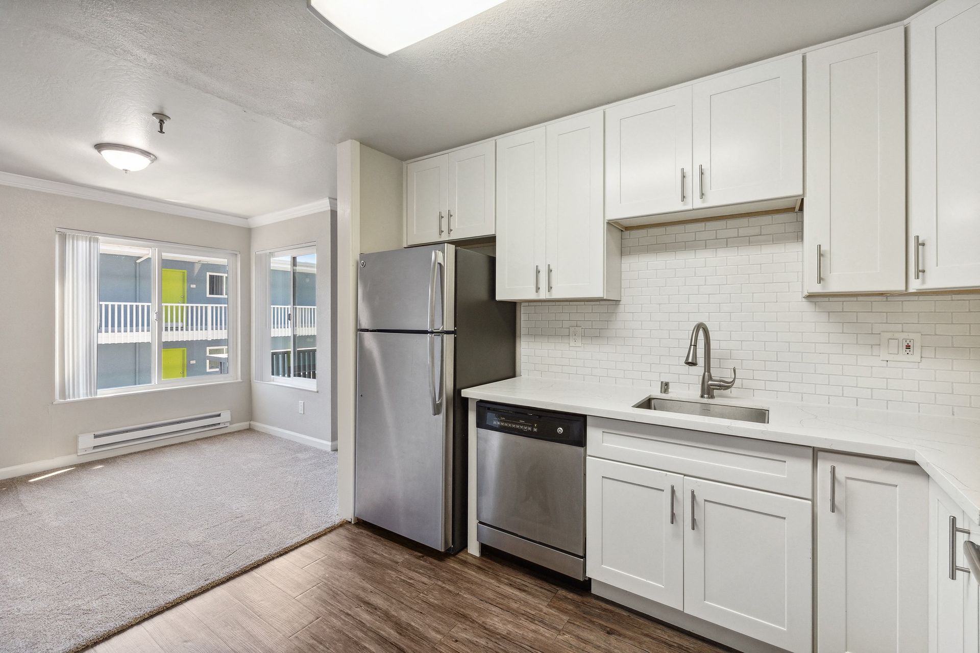 Modern apartment kitchen with white cabinets, stainless steel fridge and dishwasher, and a subway tile backsplash.
