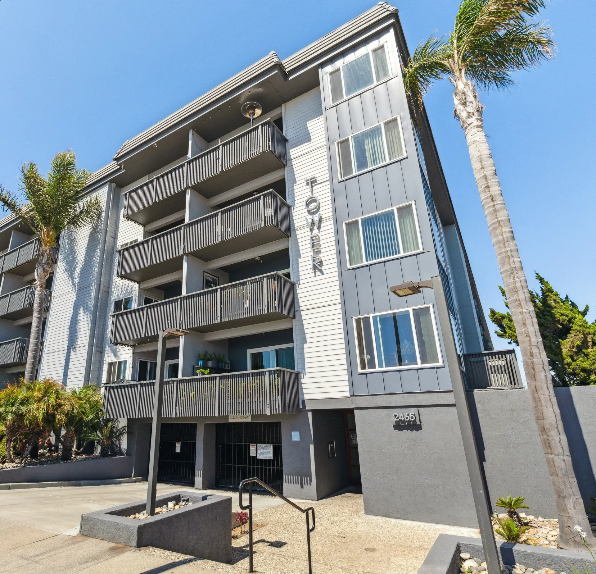 Exterior view of a modern apartment building with balconies and palm trees against a clear blue sky.