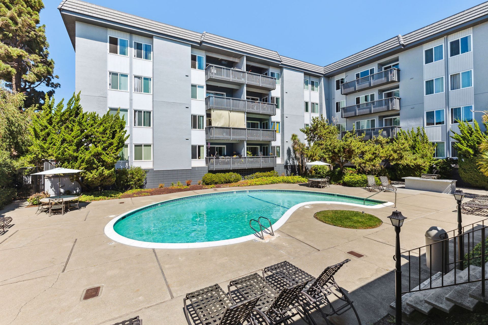 Outdoor pool area in a courtyard with lounge chairs and a gray apartment building.