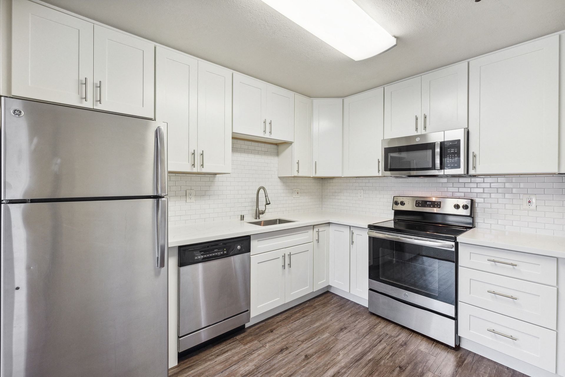 Bright white kitchen with stainless steel fridge, range, microwave, and dishwasher.