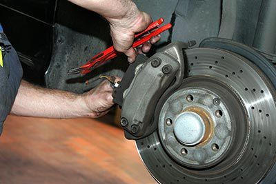 A man is working on a car brake with a pair of pliers.