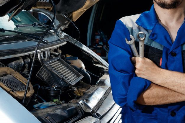 A man is holding a wrench in front of a car with the hood open.