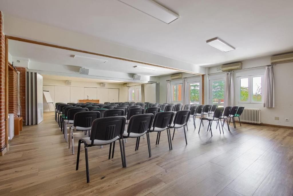 Empty conference room with black chairs facing a small stage. Windows along the side, wooden floor.