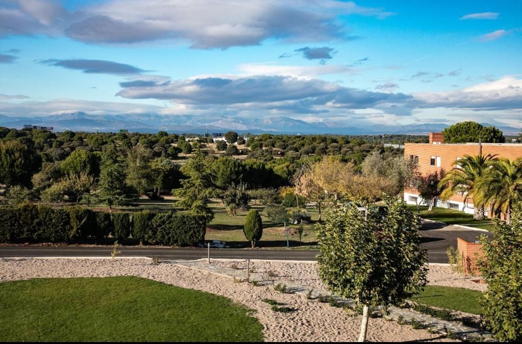 View of a green landscape with trees, a building, and mountains under a cloudy sky.