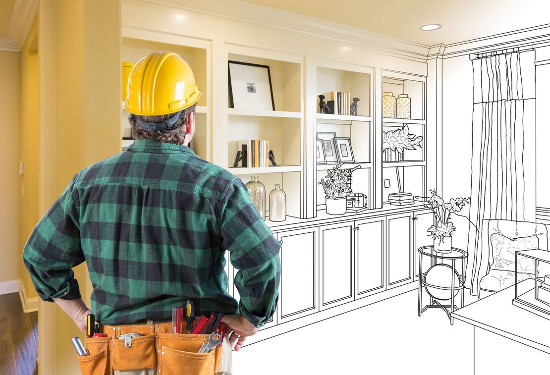 A man wearing a hard hat is standing in front of a drawing of a living room.