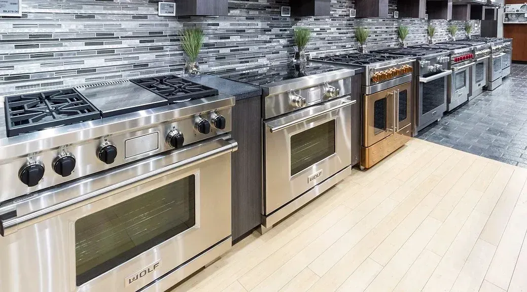 A row of stainless steel ovens are lined up in a kitchen.