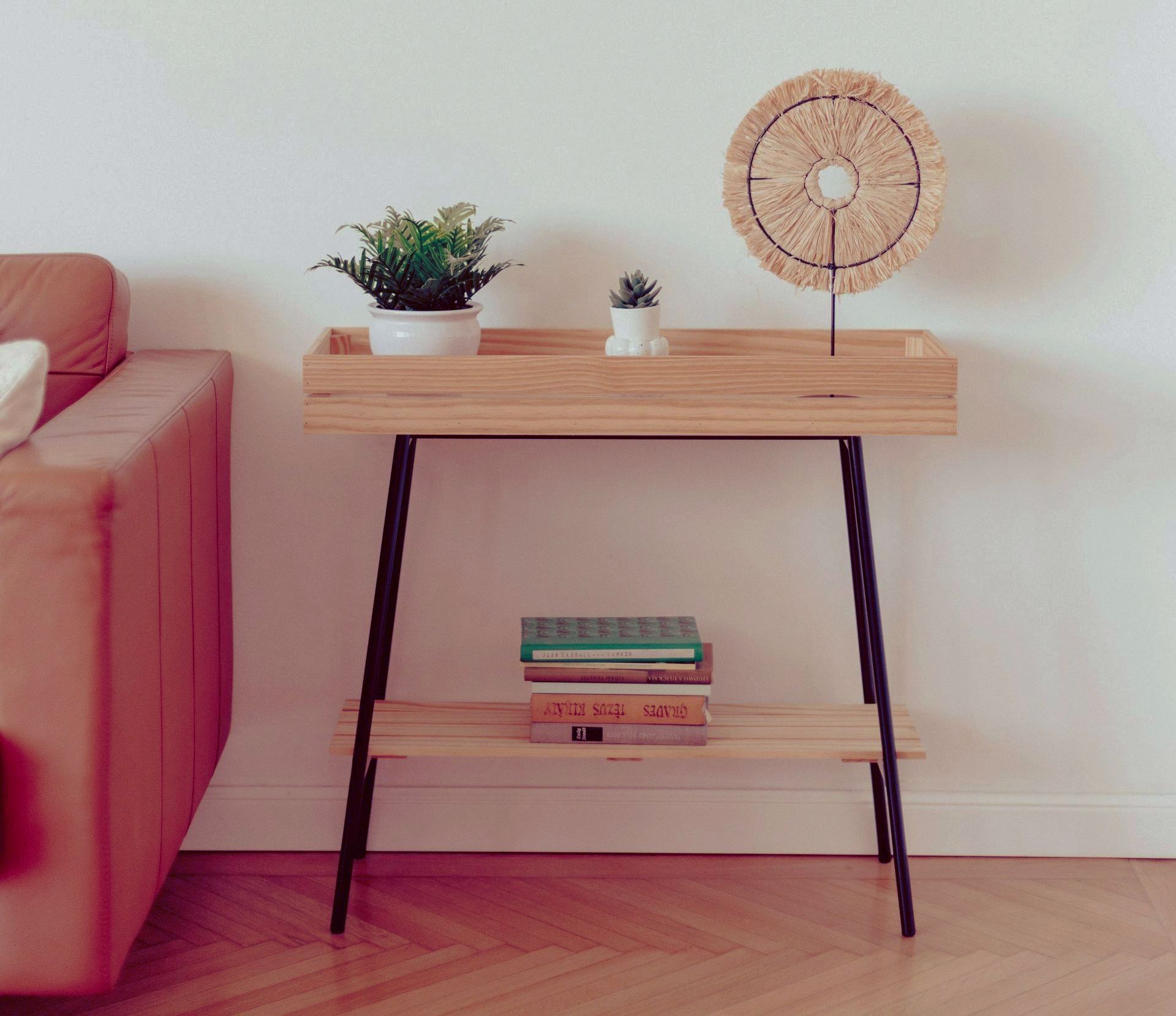 two tiered wooden side table with three books on the bottom shelf, a cactus on the top next to a tan leather couch