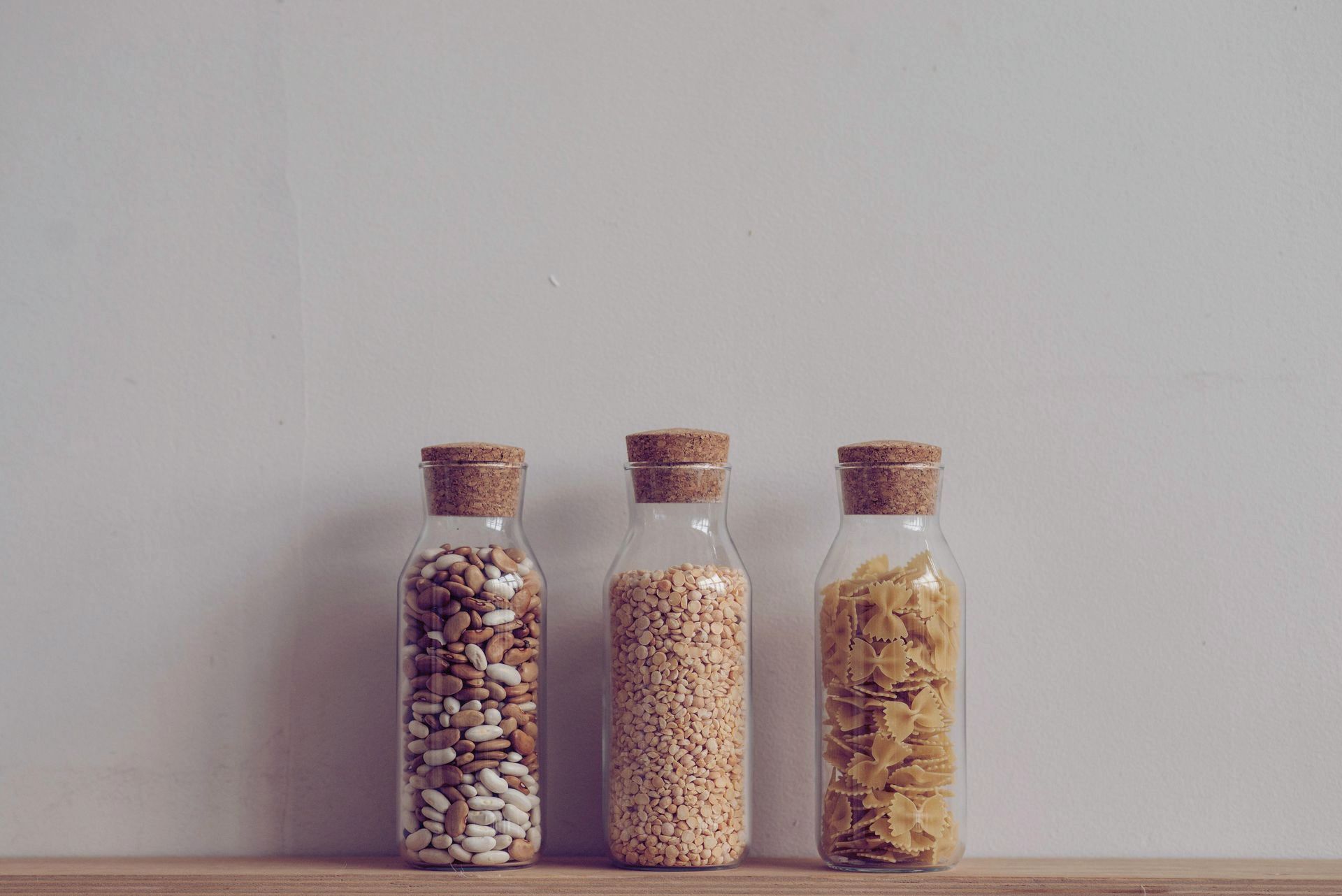 three aesthetic glass jars organised and filled with kitchen ingredients sitting on a wooden shelf