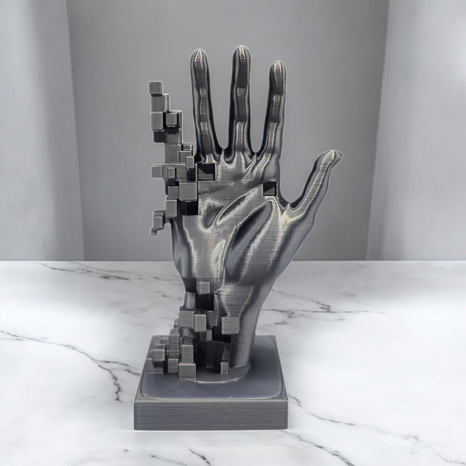Een zilverkleurig, 3D-geprint handbeeldje met een pixelachtig ontwerp, rustend op een marmeren ondergrond.