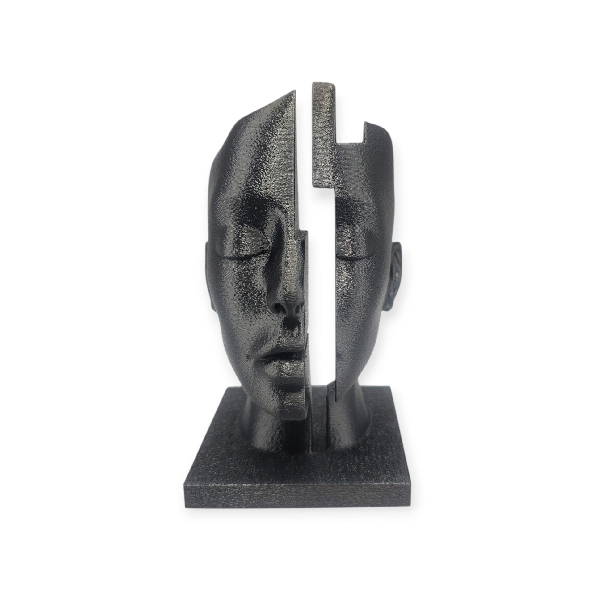 Zwarte sculptuur van een gezicht dat in twee helften is verdeeld, met gesloten ogen, op een vierkante sokkel.