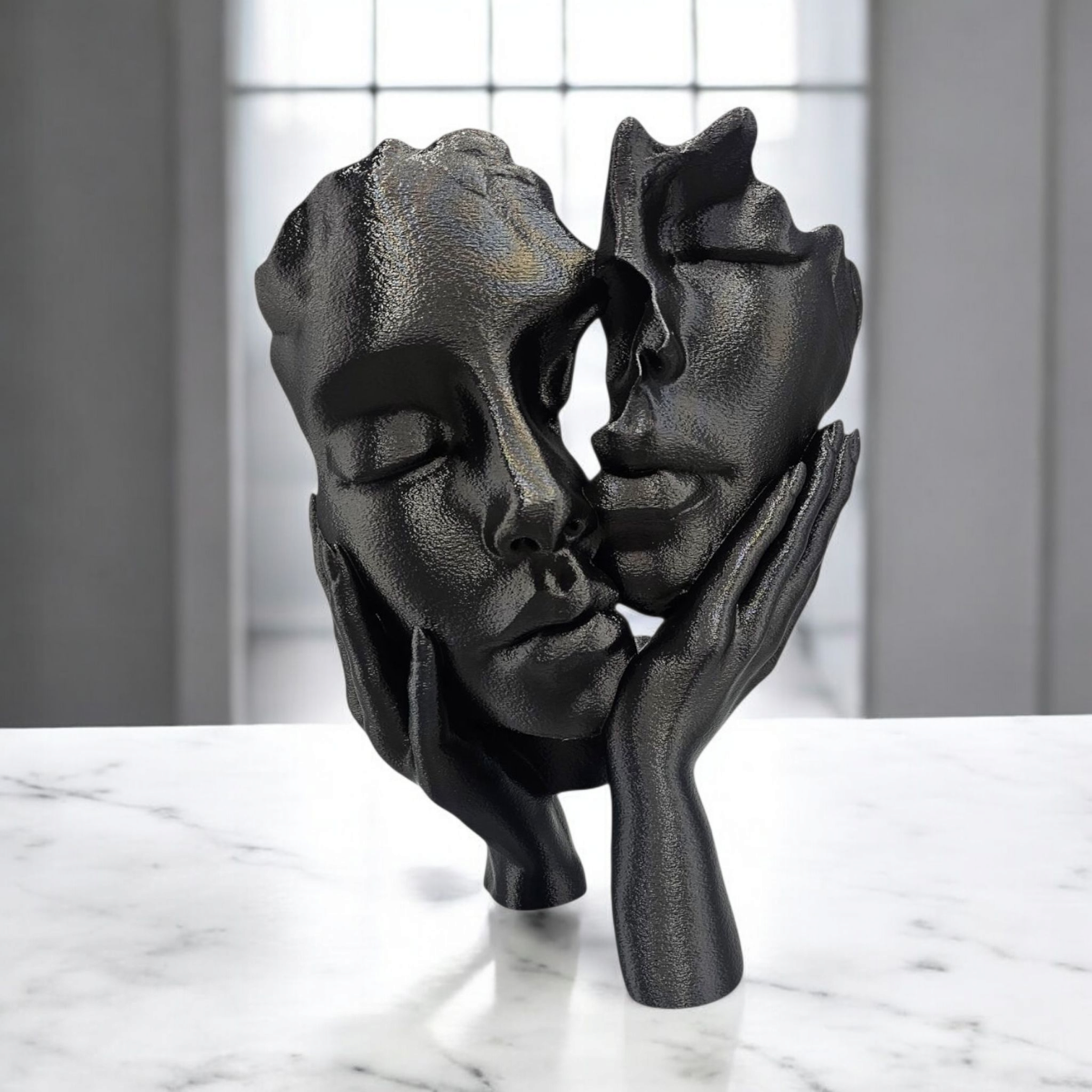 Zwarte sculptuur van twee in elkaar verstrengelde gezichten die elkaar lijken aan te raken; handen omarmen de gezichten, geplaatst op een marmeren ondergrond.
