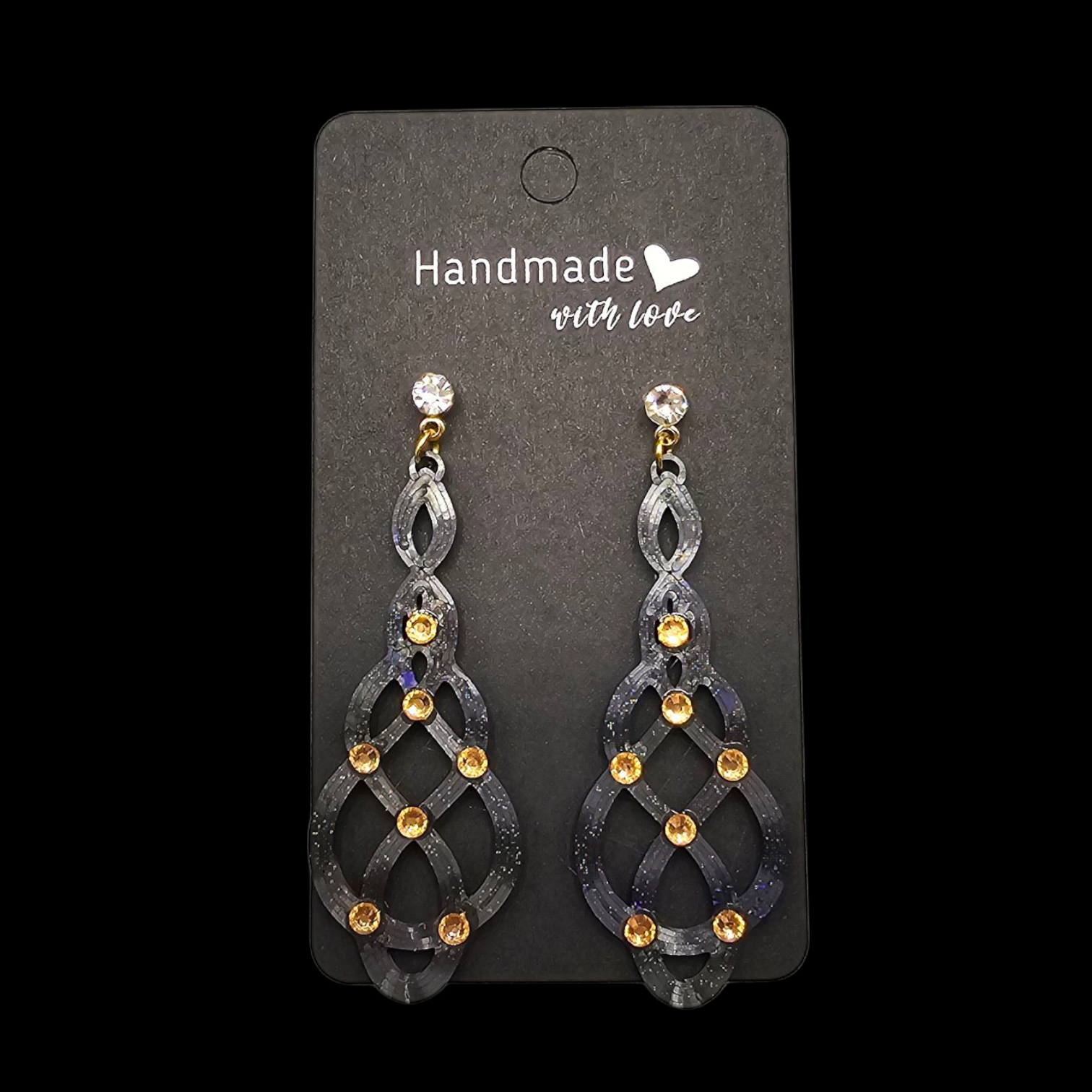 Oorbellen op een zwart kaartje, met een sierlijk zilvergrijs ontwerp, gouden accenten en een transparante steen aan de bovenkant.