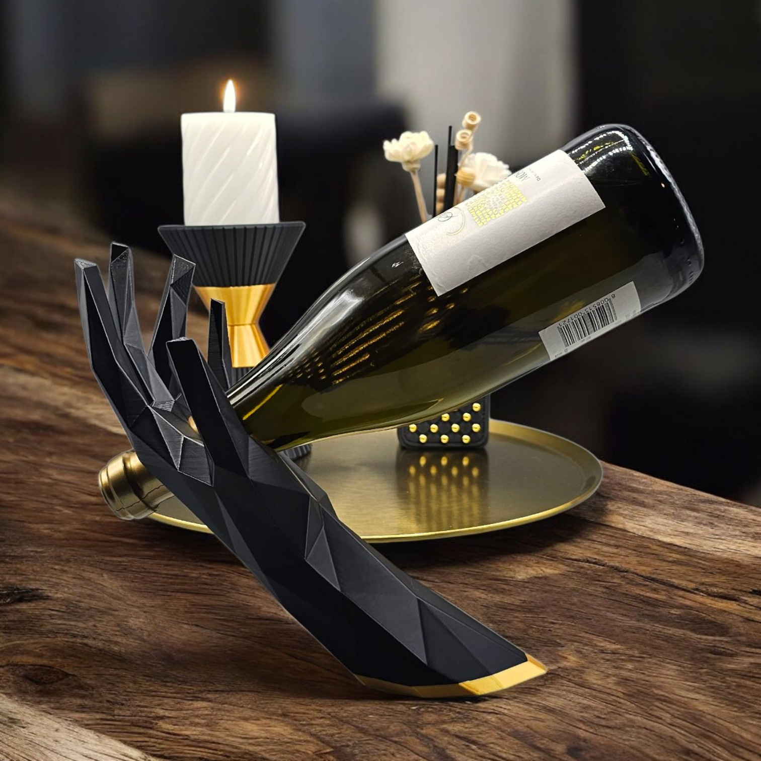 Zwarte, geometrische, handvormige wijnhouder met daarop een wijnfles op een houten tafel, met kaarsen en een dienblad op de achtergrond.