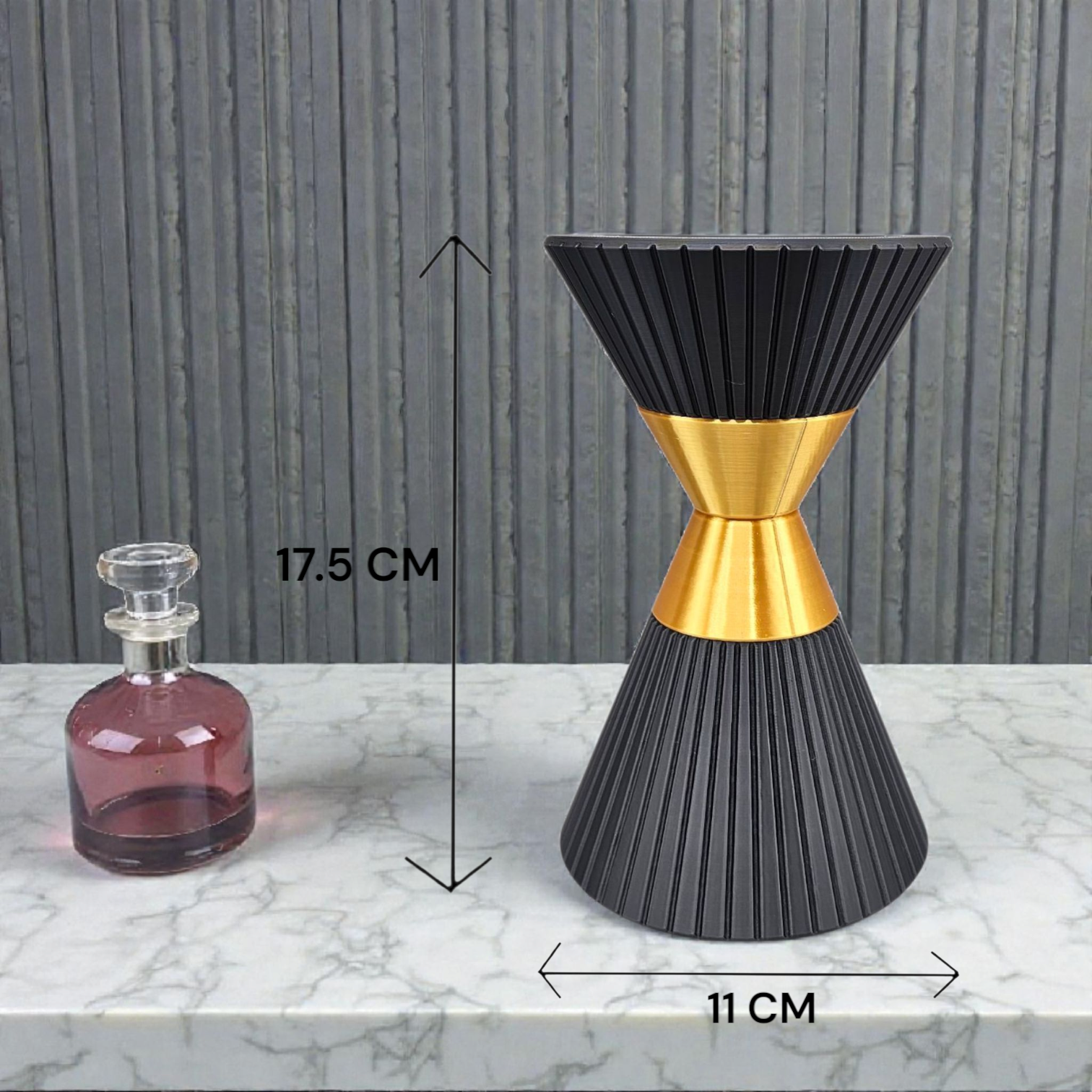 Zwarte en gouden zandlopervormige vaas, 17,5 cm hoog, met een klein roze flesje op een marmeren voetstuk.