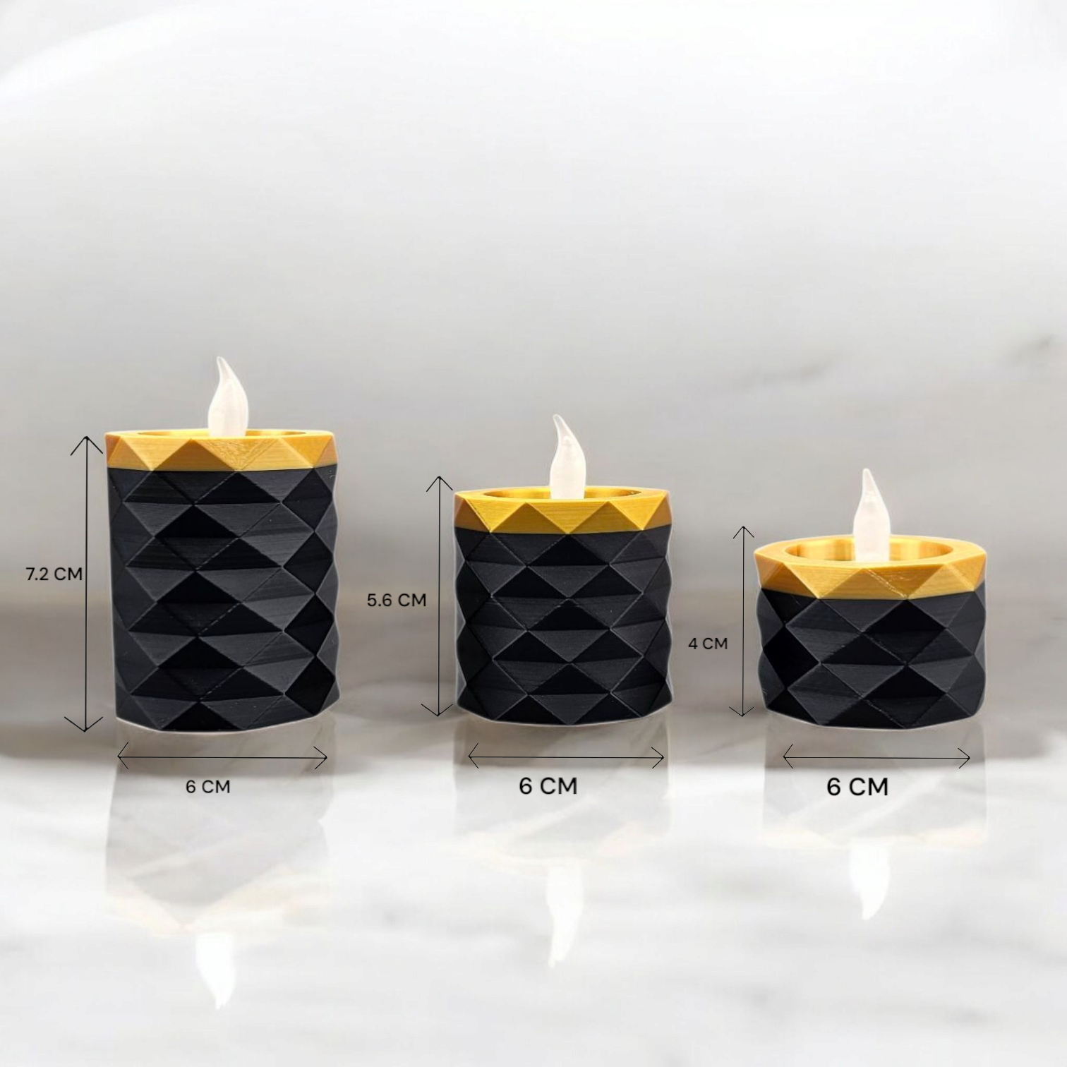 Drie geometrische LED-kaarsen in zwart en goud op een marmeren ondergrond.