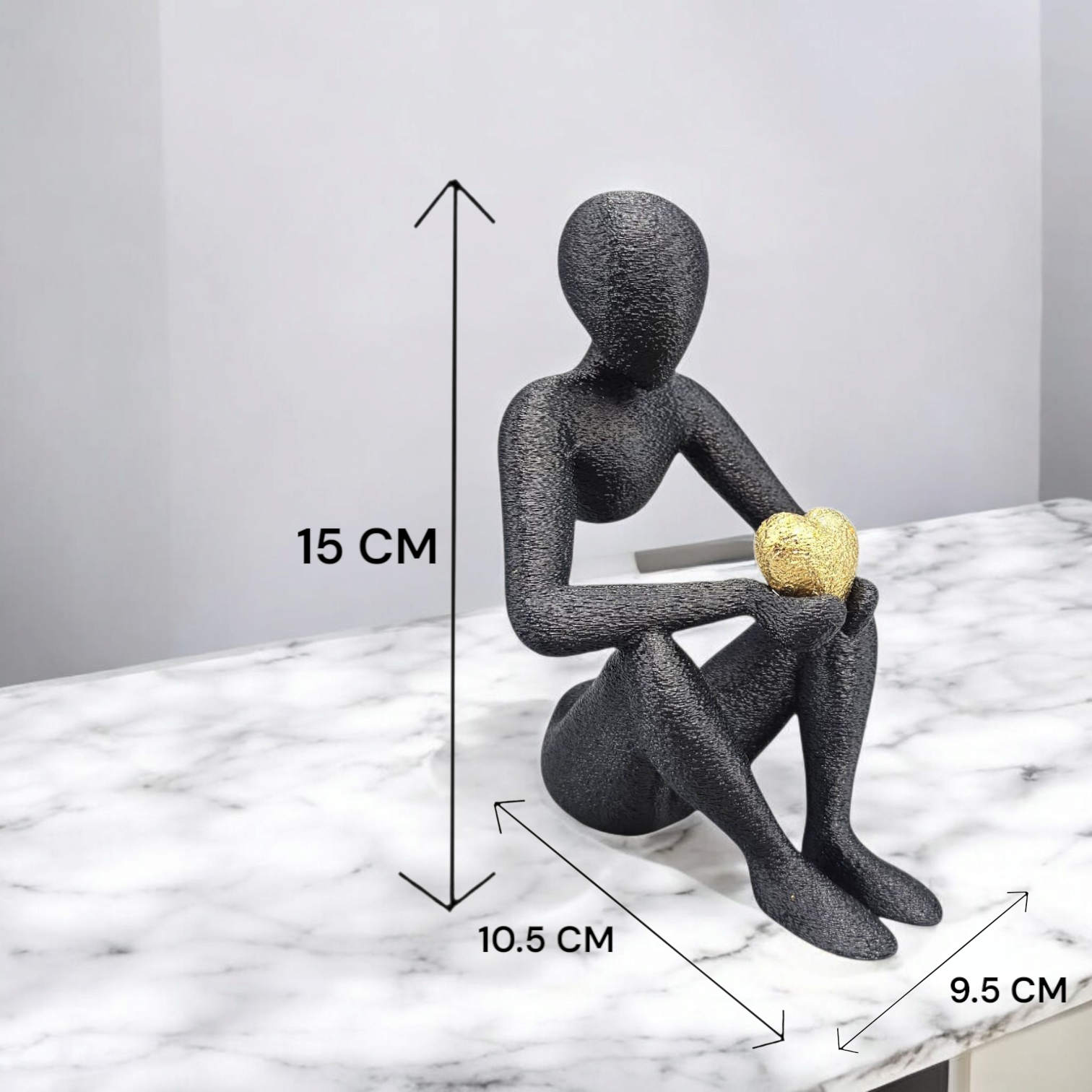 Zwart zittend beeldje, dat een gouden voorwerp vasthoudt, 15 cm hoog, op een marmeren ondergrond.