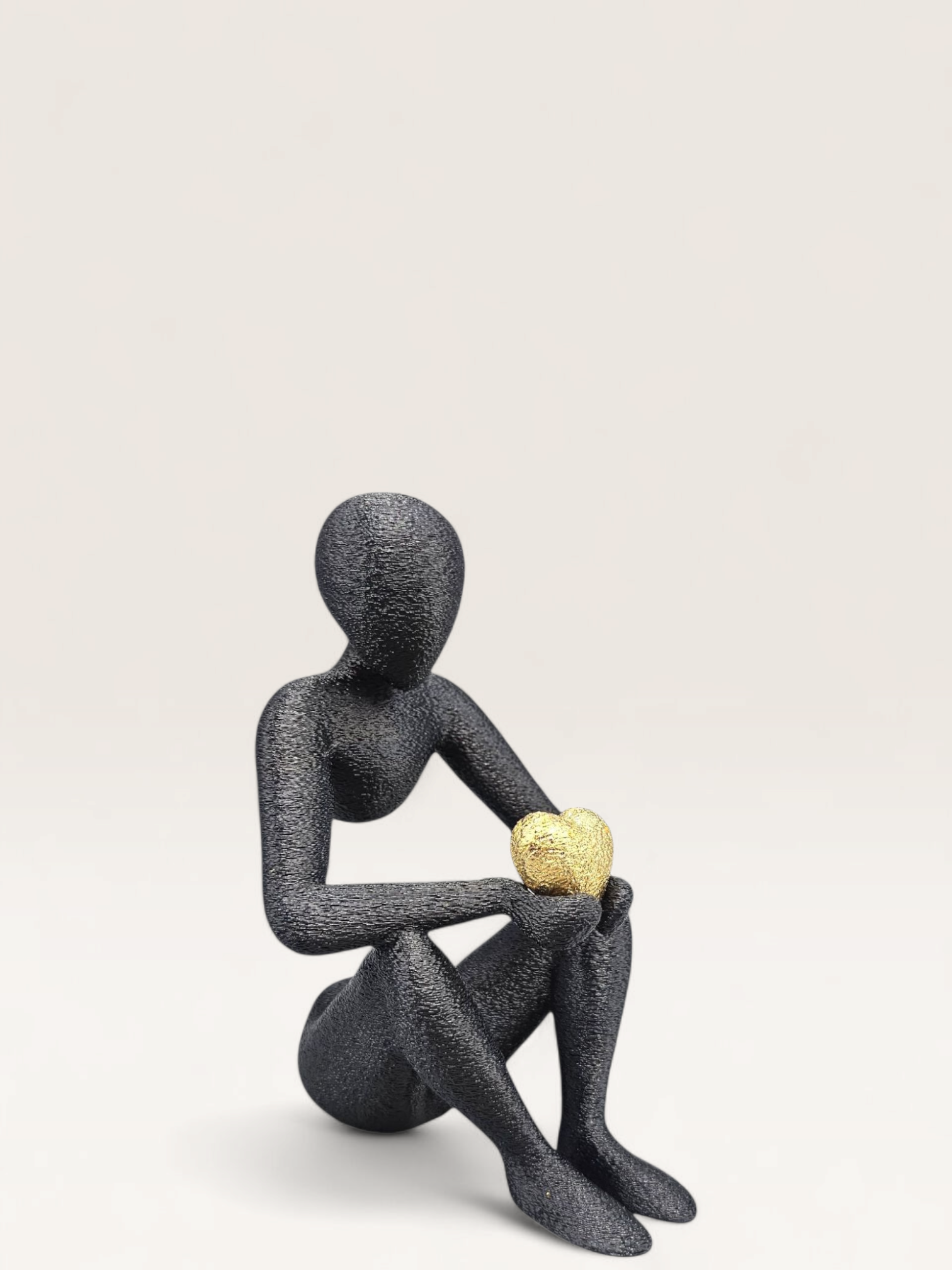 Zwart zittend beeldje, dat een gouden voorwerp vasthoudt, 15 cm hoog, op een marmeren ondergrond.