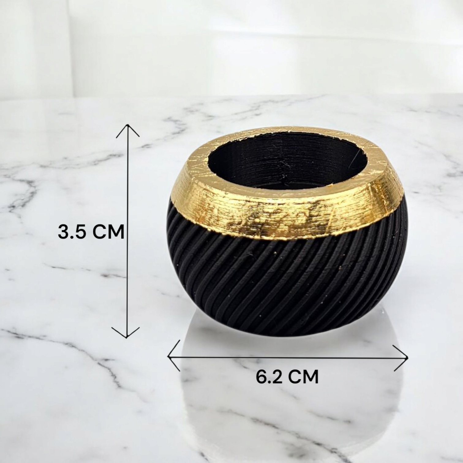 Cilindrische plantenbak in zwart en goud met diagonale ribbels, afmetingen 3,5 cm x 6,2 cm, op een marmeren ondergrond.