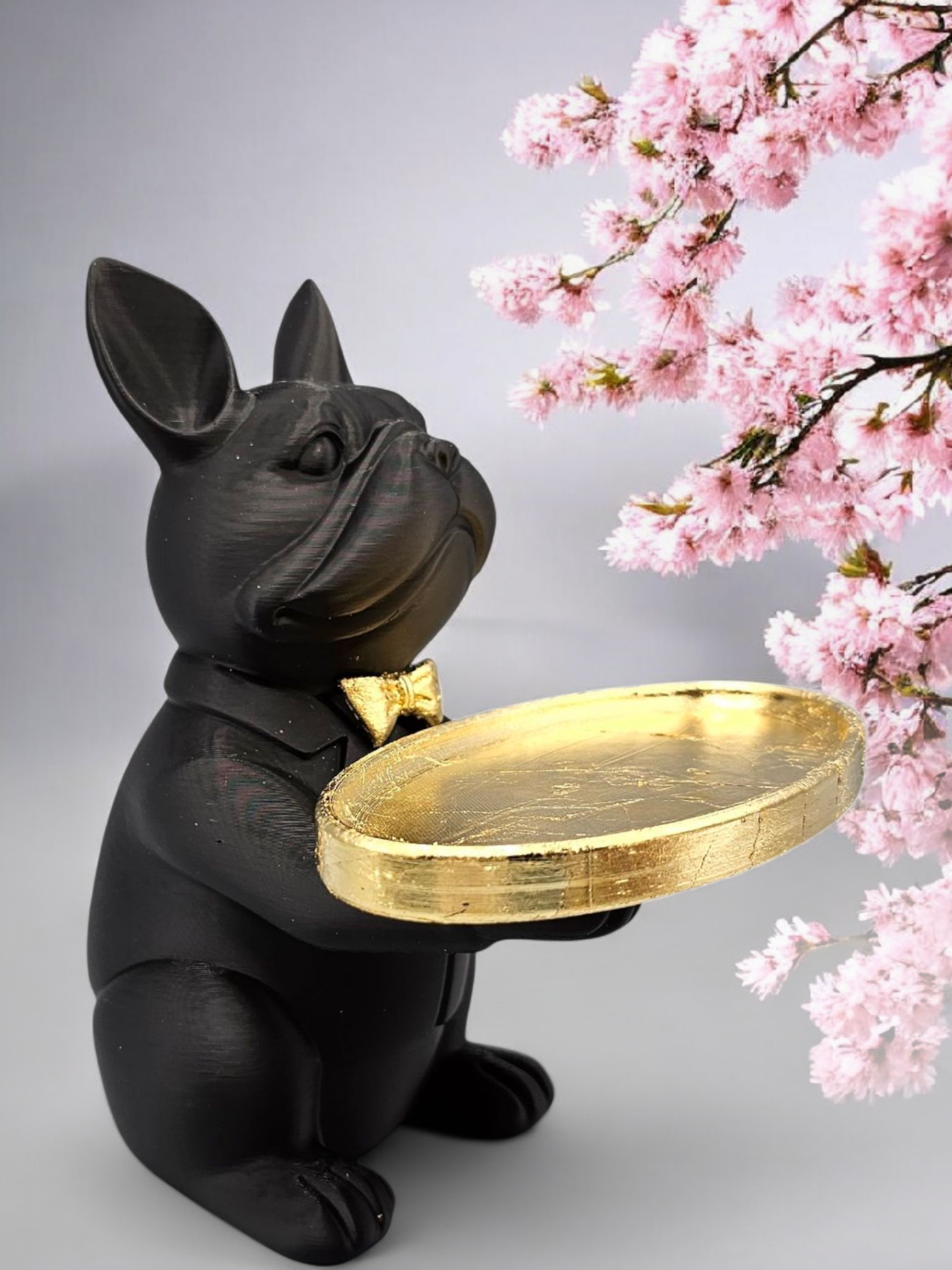 Een beeld van een zwarte bulldog die een gouden dienblad vasthoudt, met op de achtergrond roze kersenbloesemtakken.